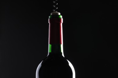 Opening wine bottle with corkscrew on dark background, closeup