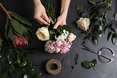 Florist making beautiful bouquet at black table, top view