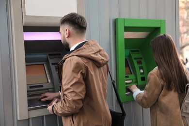 Photo of Young man using cash machine for money withdrawal outdoors