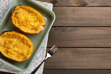 Halves of cooked spaghetti squash in baking dish and fork on wooden table, flat lay. Space for text