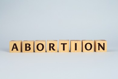 Word Abortion made of wooden cubes on light grey background