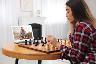 Young woman playing chess with partner via online video chat at home