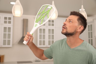 Photo of Man with electric fly swatter in kitchen. Insect killer