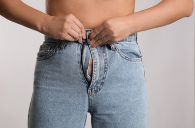 Woman trying to put on tight jeans against light background, closeup