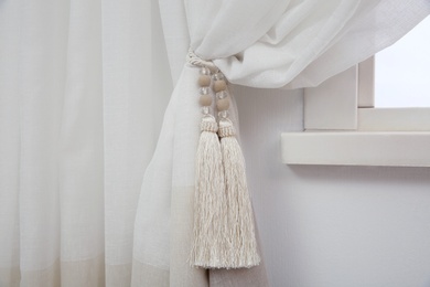 Photo of Elegant window curtain with tieback in room, closeup