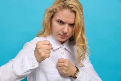 Angry young woman ready to fight on light blue background