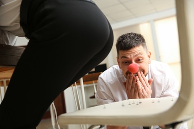Man putting pins on chair while his colleague sitting down in office, closeup. Funny joke