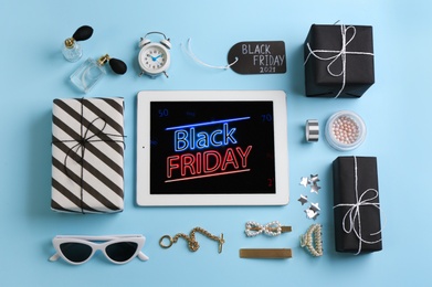 Flat lay composition with tablet, gifts and accessories on light blue background. Black Friday sale