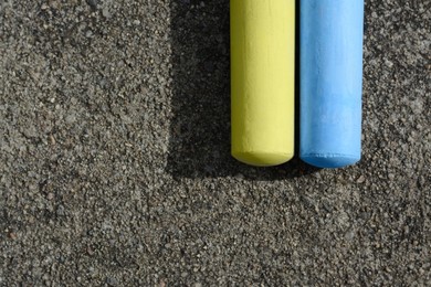 Yellow and light blue chalk sticks on asphalt, flat lay. Space for text