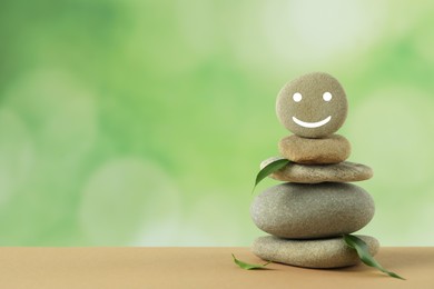 Stack of stones with drawn happy face and green leaves on table against blurred background, space for text. Zen concept
