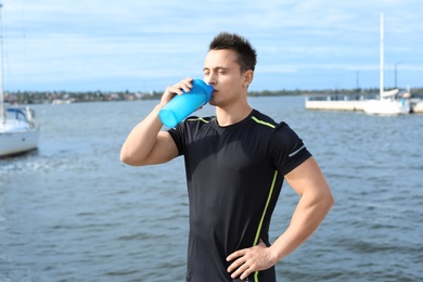 Young man drinking protein shake near river