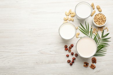 Different vegan milks and nuts on white wooden table, flat lay. Space for text