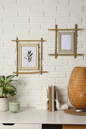 Photo of Potted houseplant, decor elements and books on white table near brick wall with stylish bamboo frames