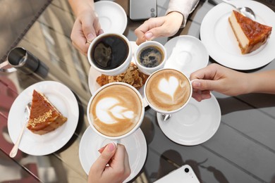 Photo of Friends drinking coffee at wooden table in outdoor cafe, top view