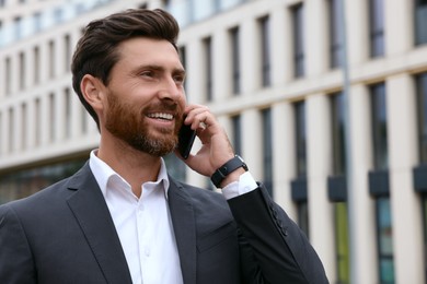 Handsome businessman talking on smartphone while walking outdoors, space for text