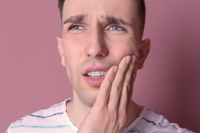 Young man with sensitive teeth on color background, closeup