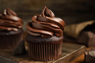 Delicious chocolate cupcakes with cream on wooden board, closeup