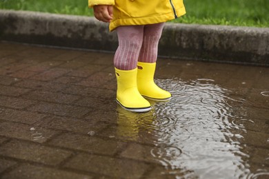 Girl walking in puddle outdoors on rainy weather, closeup
