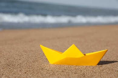 Yellow paper boat near sea on sandy beach, space for text