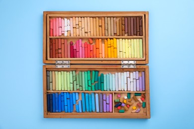 Set of soft pastels in wooden box on light blue background, top view. Drawing material