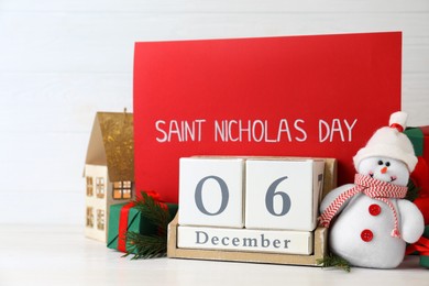 Photo of Saint Nicholas Day. Block calendar with date December 06, red card and festive decor on white wooden table