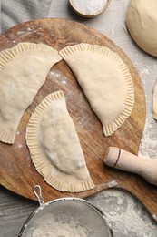 Photo of Raw chebureki with tasty filling and rolling pin on wooden table, flat lay