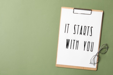 Clipboard with phrase It Starts With You and glasses on green background, flat lay. Space for text