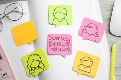 Sticky notes with words Diversity, Equality, Inclusion and drawings of people on wooden table, flat lay