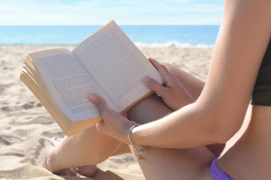 Woman reading book on sandy beach near sea, closeup