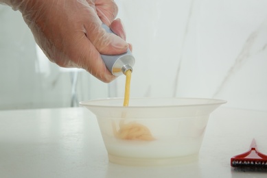 Woman preparing hair dye in bowl at white table, closeup