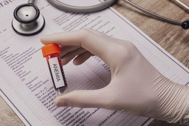Doctor holding test tube with blood sample and label Anemia over table, closeup