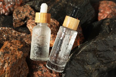 Bottles of face serum on wet stones, closeup
