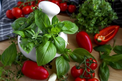 Photo of Mortar with fresh herbs, cherry tomatoes and pepper on wooden table, closeup