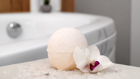 Bath bomb with orchid and sea salt on table in bathroom