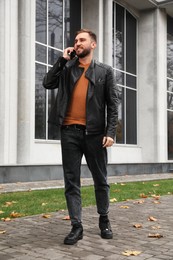 Handsome man in stylish leather jacket talking on mobile phone outdoors