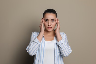 Young woman suffering from headache on beige background