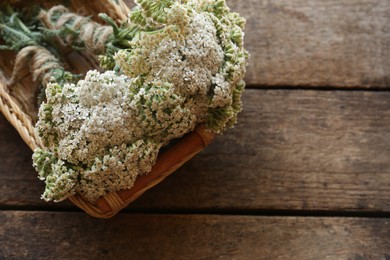 Photo of Basket with bunches of beautiful dries yarrow on wooden table, top view. Space for text