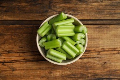 Cut celery in bowl on wooden table, top view