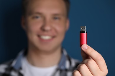 Man with usb flash drive against blue background, focus on device. Space for text