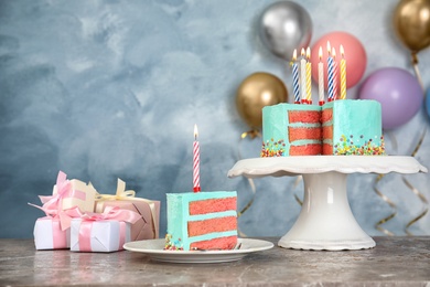 Fresh delicious cake with candles and gifts on table against color background