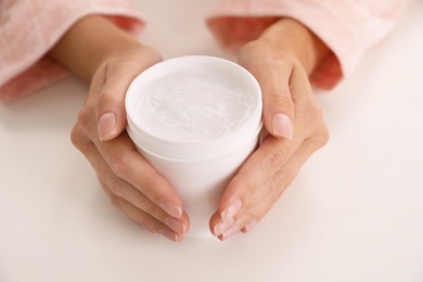 Woman with jar of moisturizing cream at white table, closeup