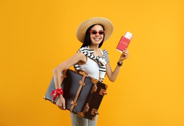 Happy female tourist with passport, ticket and suitcase on yellow background
