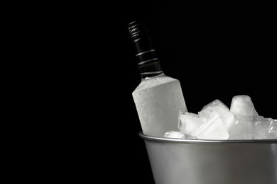 Bottle of vodka in metal bucket with ice on black background. Space for text