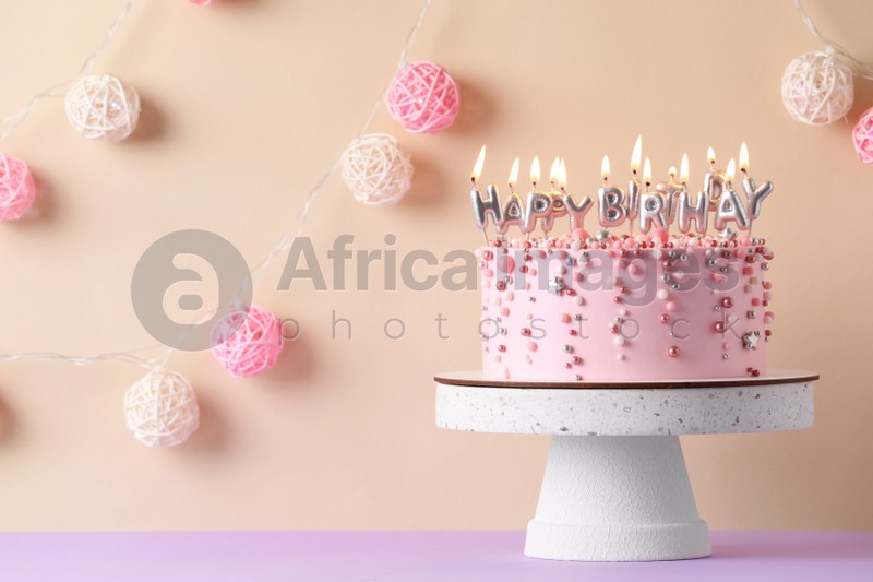Birthday cake with burning candles on violet table, space for text