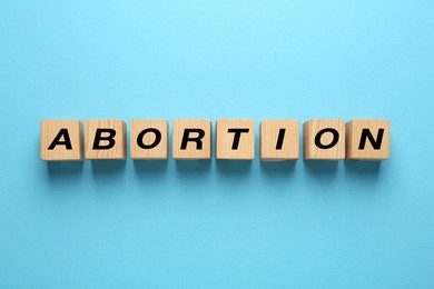 Word Abortion made of wooden cubes on light blue background, flat lay