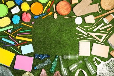 Flat lay composition with household goods on green grass, space for text. Recycling concept