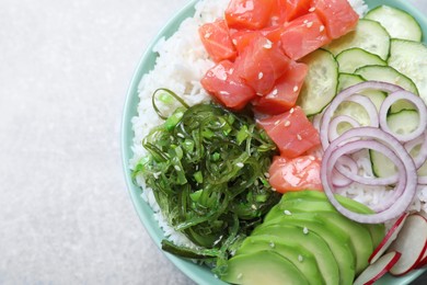 Delicious poke bowl with salmon, seaweed and vegetables on light grey table, top view