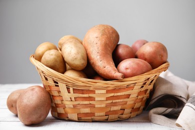 Photo of Different types of fresh potatoes in wicker basket on white wooden table