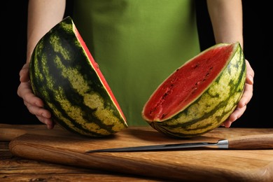 Woman with delicious halved watermelon at wooden table against black background, closeup