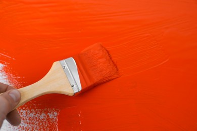 Man applying orange paint with brush on white background, closeup